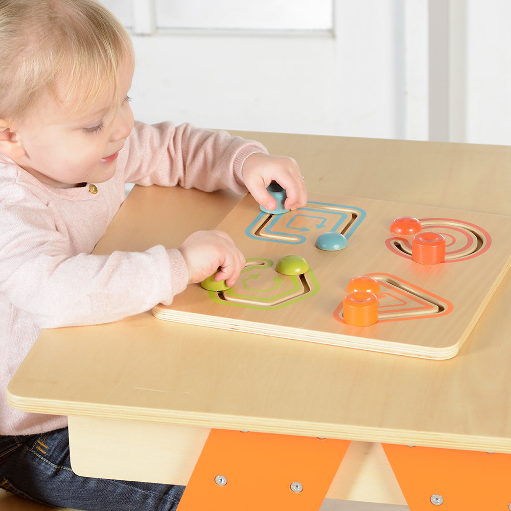 Toddler sliding geometric shapes along track for early development activities.