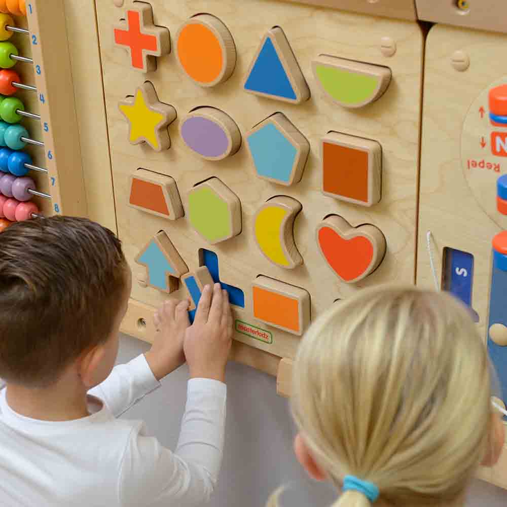 Children matching magnetic shapes on wooden activity wall board.