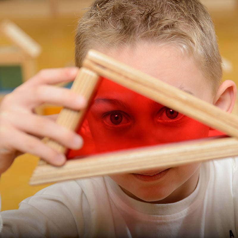 Child holding a rainbow block and observing the world through tinted acrylic.