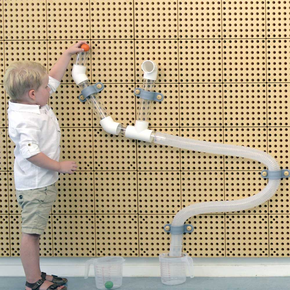 Children building a ball run on a Masterkidz STEM Wall using flexible and rigid tubes.