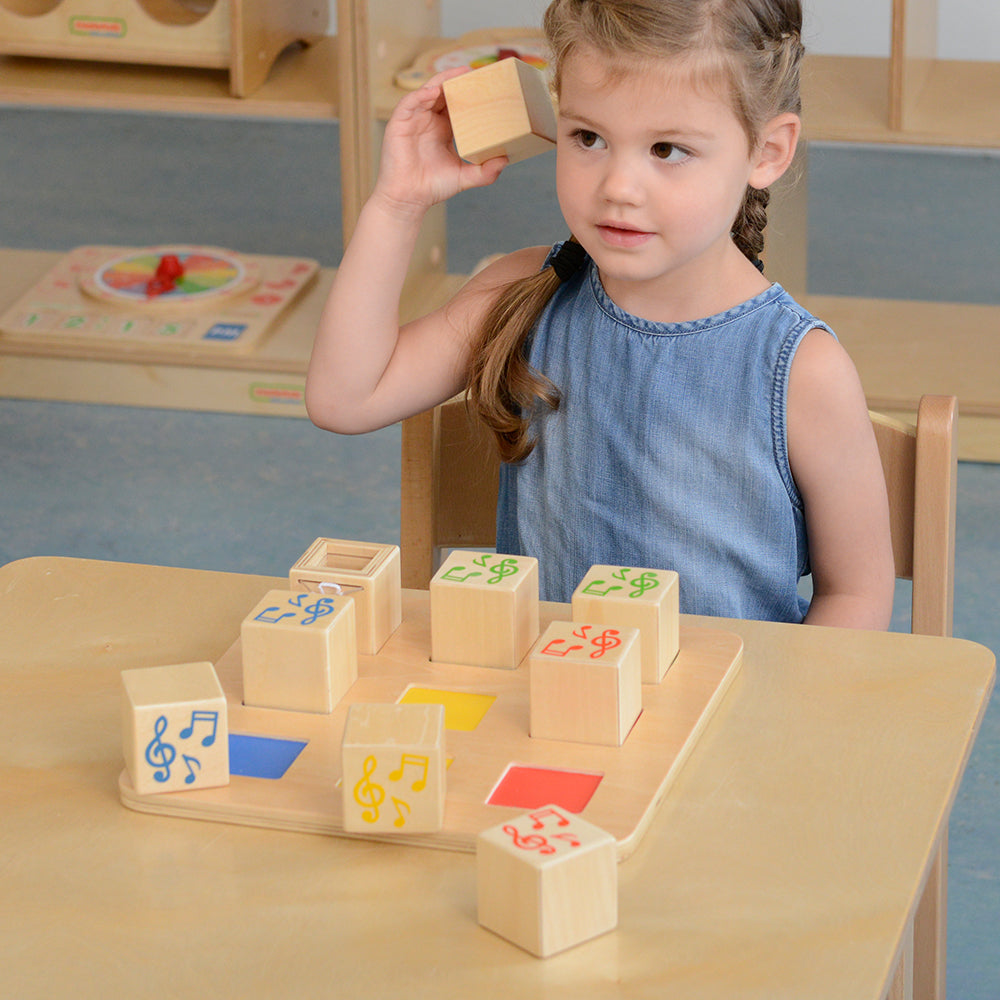 Child shaking cubes to identify and match sounds during sensory learning play.