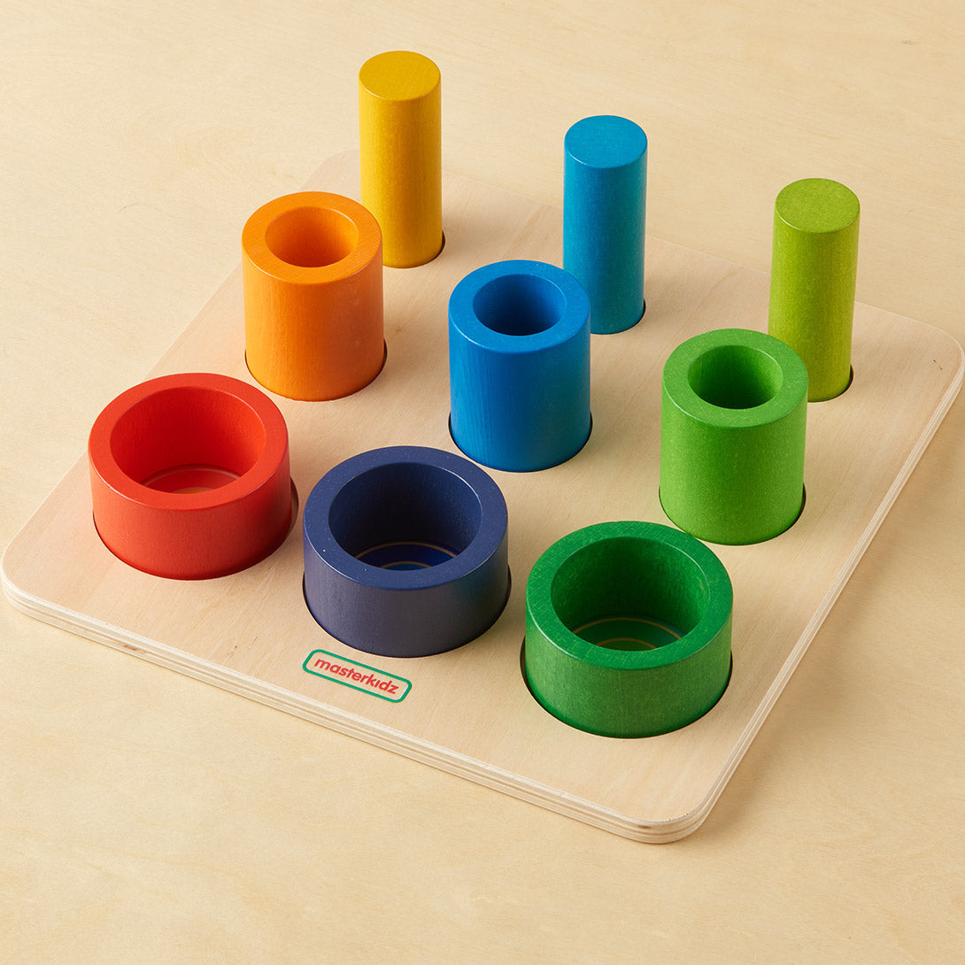 A child lifting a brightly coloured wooden tube to explore its texture and shape.